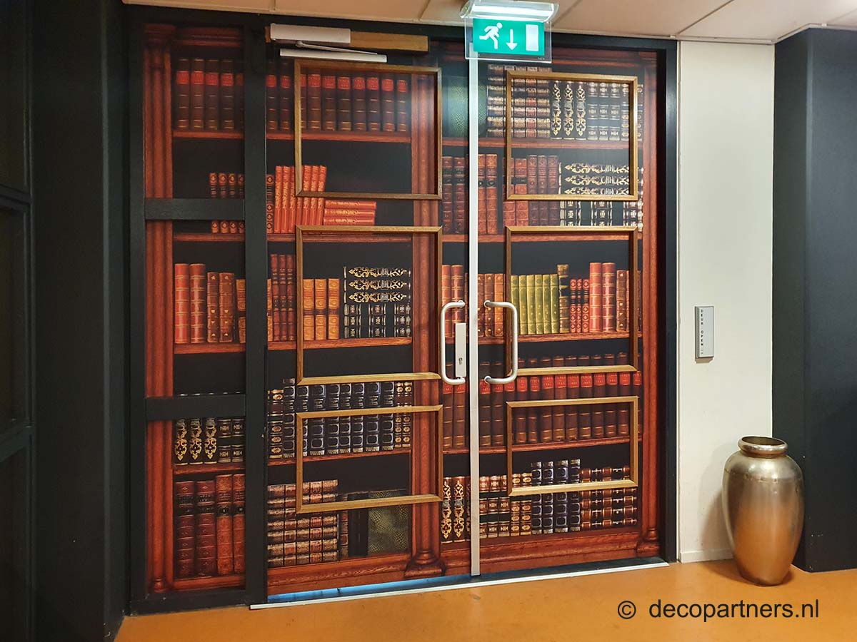 Deze entree bij een zorginstelling is decoratief uit het zicht gehaald met een mooie boekenkast-print voor mensen met dementie zodat er meer rust op de afdeling komt