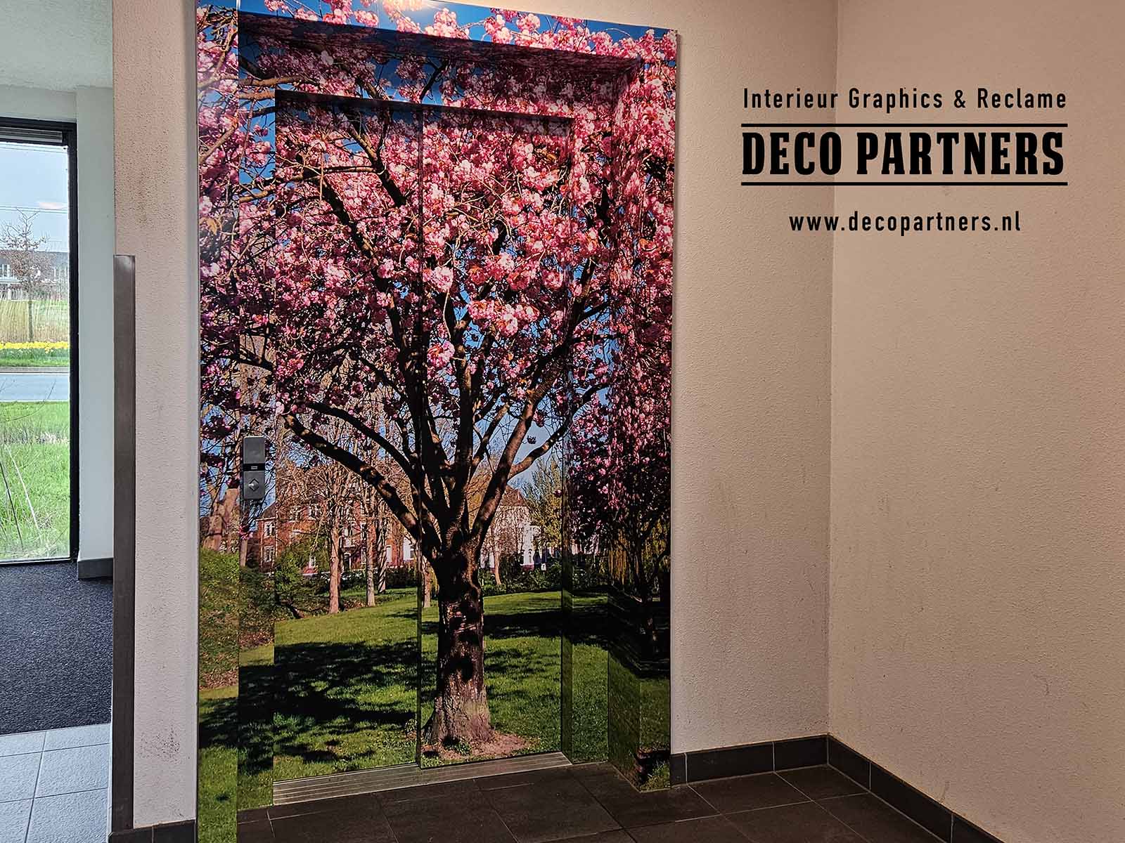 De liftdeuren en omlijsting zijn volledig voorzien van hoogwaardige interieurfolie met een sfeervolle bloesemprint. Het ontwerp laat de lift opgaan in de wand en zorgt voor een frisse en natuurlijke uitstraling in de ruimte. De liftwrapping is afgewerkt met een transparante anti-graffiti beschermlaag, waardoor verf en inkt van stiften zich nauwelijks hechten en eenvoudig te verwijderen zijn. Zo blijft de lift er langer netjes uitzien en is het oppervlak onderhoudsvriendelijk.