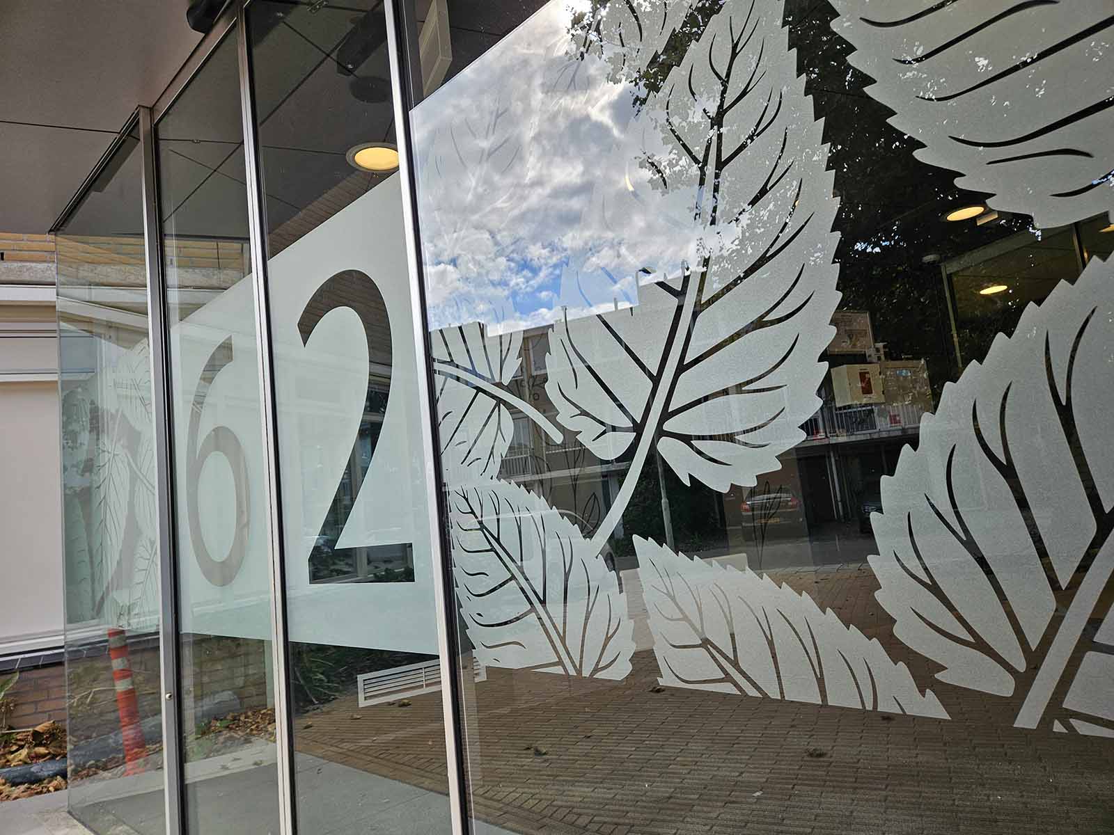Matglasfolie met bladerenpatroon en huisnummer op entree van zorginstelling